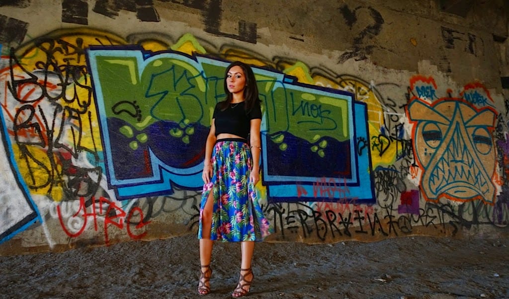 Blogger Nihan posing in front of a graffiti wall and showing her outfit: a floral midi skirt by Topshop and a black crop top