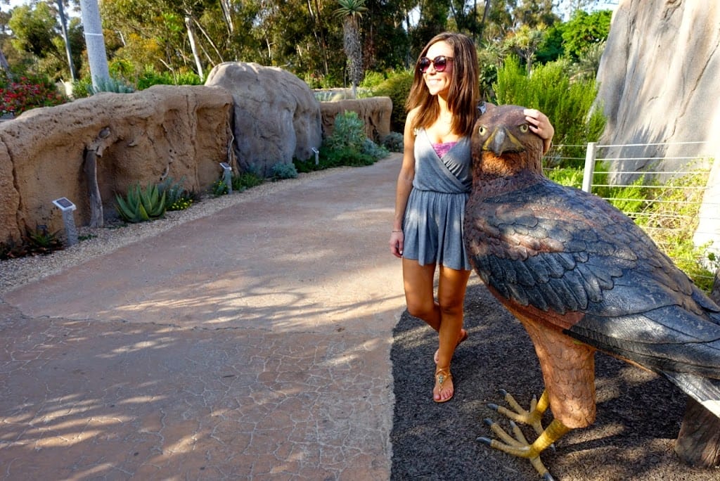 Blogger Nihan posing with a bird sculpture and showing her outfit, a casual grey romper at the San Diego Zoo