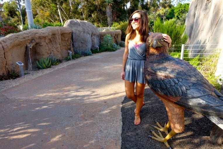 Blogger Nihan posing with a bird sculpture and showing her outfit, a casual grey romper at the San Diego Zoo