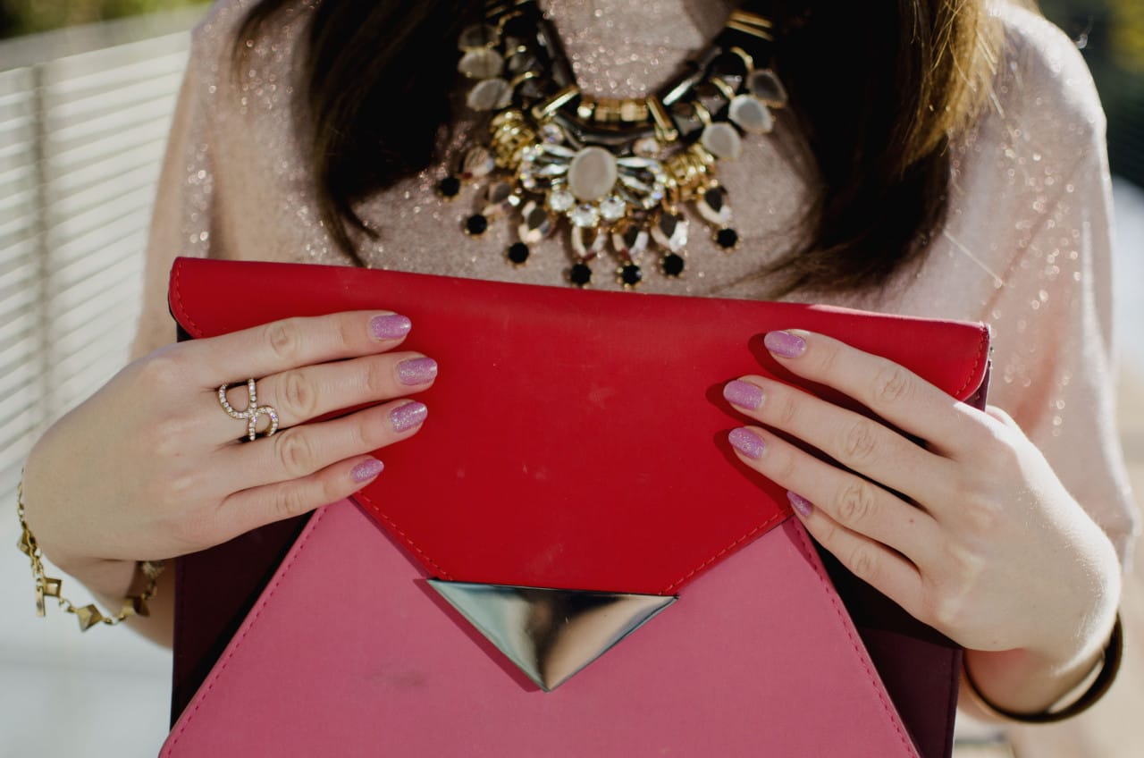 Blogger Nihan showing her rings, pink glittery nails and pink and red color block festive clutch
