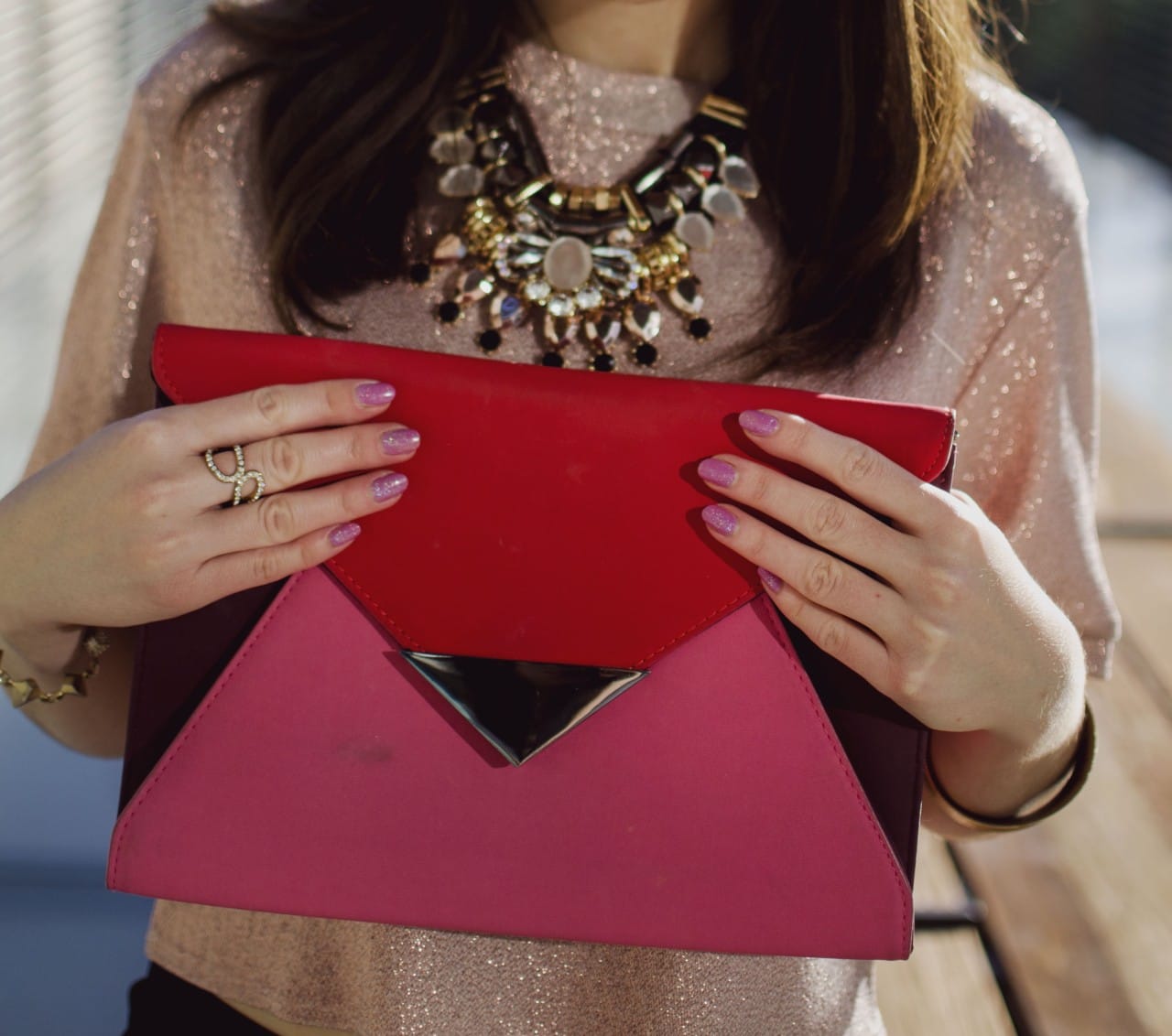 elegant holiday party look - Blogger Nihan showing her rings, necklace, pink glittery nails and pink and red color block festive clutch