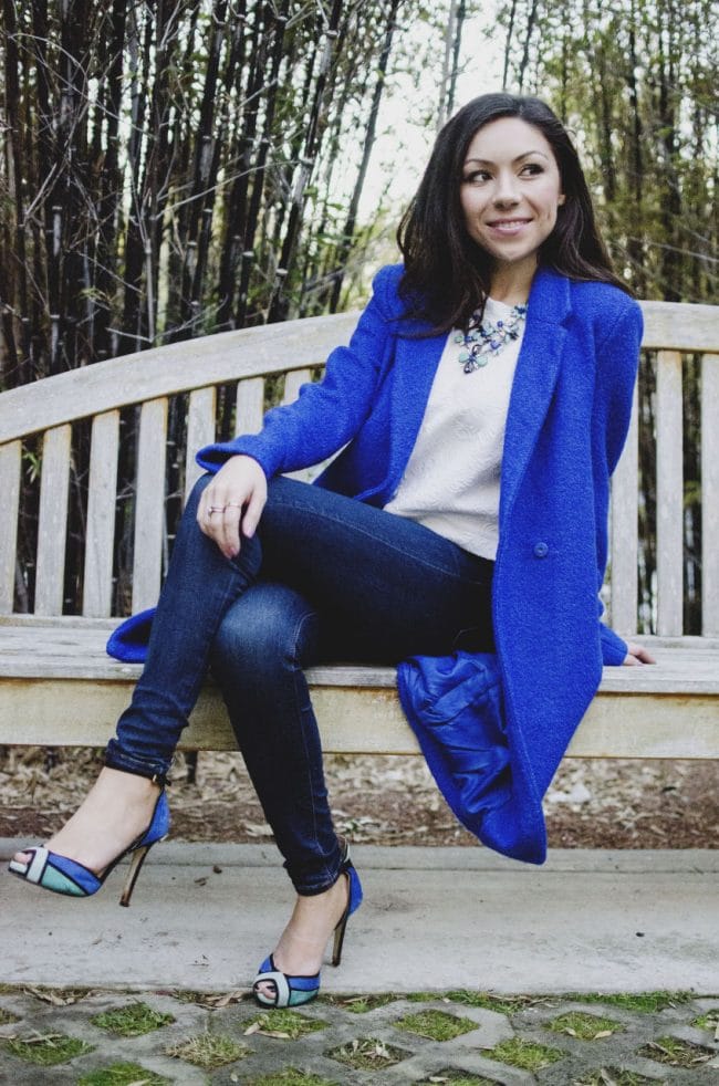 Nihan wearing a cobalt blue coat and posing while sitting on a bench
