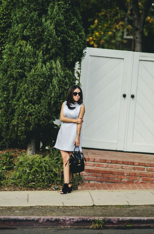 Nihan Gorkem wearing baby blue mod dress black and gold backpack black open toe booties and jewelry, posing in front of a cute white door - - winter baby blues