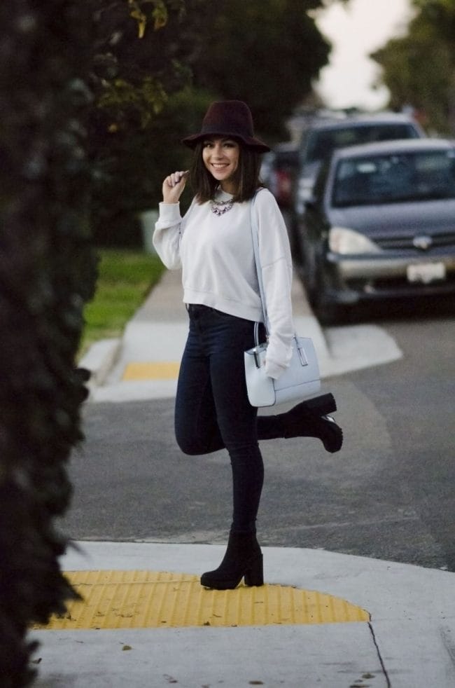 Nihan smiling and posing in Bird Rock San Diego, wearing a Topshop white sweatshirt, Topshop skinny jeans and River Island Blue Tote Bag