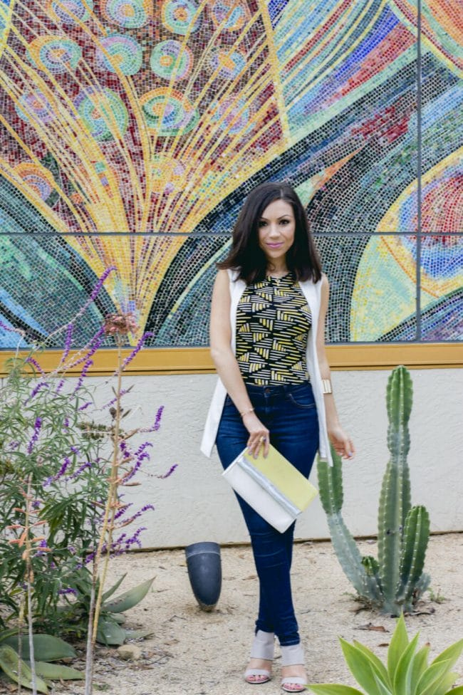 Nihan Gorkem posing in a cactus garden wearing a Topshop white sleeveless jacket, Topshop printed top, blue high-waisted jeans and a colorblock clutch from H&M
